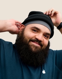 Retrato de una persona del equipo de Apple Retail sonriendo, con barba completa y gorro tejido.