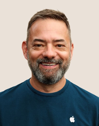 Retrato de una persona del equipo de Apple Retail sonriendo con pelo corto gris y barba.