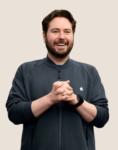 Retrato de una persona del equipo de Apple Retail sonriendo con cabello corto oscuro ondulado y barba.