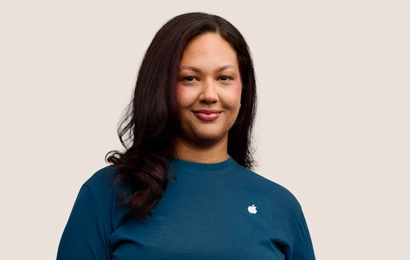 Retrato de una persona del equipo de Apple Retail sonriendo con cabello largo oscuro.
