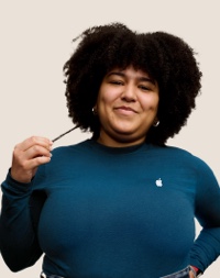 Retrato de una persona del equipo de Apple Retail sonriendo con cabello largo, rizado y oscuro.