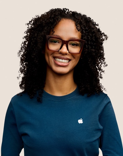 Retrato de una persona del equipo de Apple Retail sonriendo con cabello largo, rizado y oscuro y lentes.