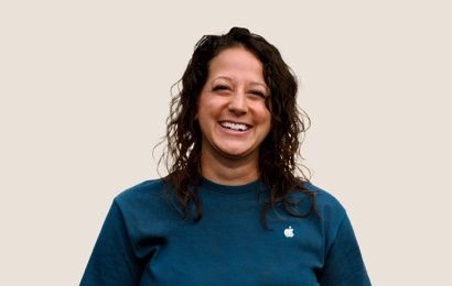 Retrato de una persona del equipo de Apple Retail sonriendo con cabello largo, ondulado y oscuro.