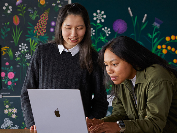 Dwie osoby z zespołu Marketing firmy Apple przy wspólnej pracy na MacBooku przed plakatami zaprojektowanymi przez ich zespół.