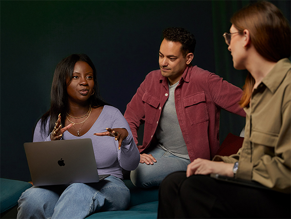 Trzy osoby z zespołu Software and Services firmy Apple rozmawiają ze sobą, siedząc na kanapie. Jedna osoba ma MacBooka.
