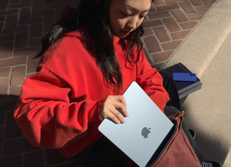 Eine Person, die auf Steinstufen sitzt, legt ein MacBook in den Rucksack.