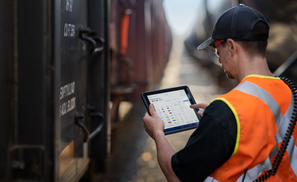 Uma pessoa que trabalha na ferrovia, ao lado de um trem, verifica um cronograma mostrado no iPad