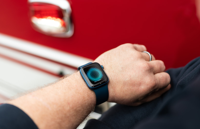 消防車の近くで、腕に着用したApple Watchに「Now inhale」というメッセージが表示されている
