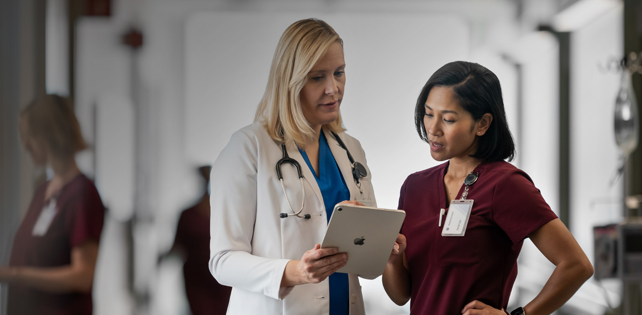Une médecin et une infirmière consultent l’écran d’un iPad dans un couloir d’hôpital.
