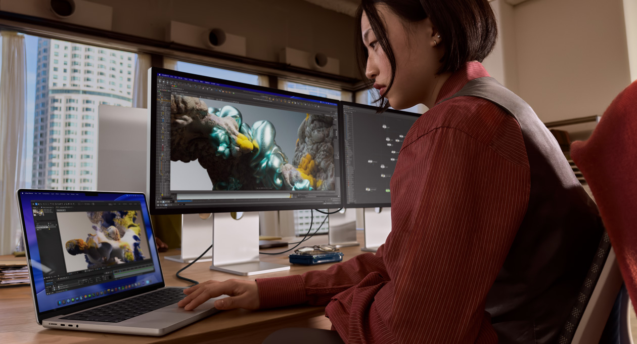 Uma pessoa em um escritório trabalha em um notebook MacBook conectado ao Studio Display XDR por uma porta Thunderbolt 5
